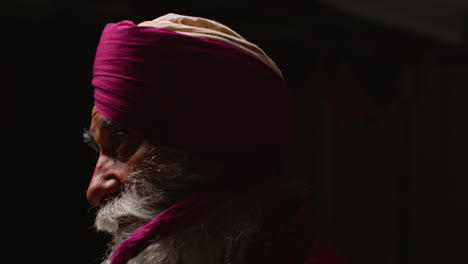 Close-Up-Low-Key-Studio-Lighting-Shot-Of-Senior-Sikh-Man-With-Beard-Tying-Fabric-For-Turban-Against-Dark-Background